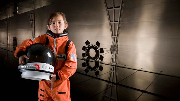 Young girl in orange space suit holding an astronaut helmet