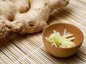 A ginger root and chopped ginger in a small bowl on a bamboo mat. With a closeup view.