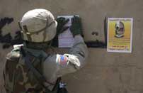 A soldier posts flyers over graffiti on a wall in Iraq as part of a Psychological Operations mission.