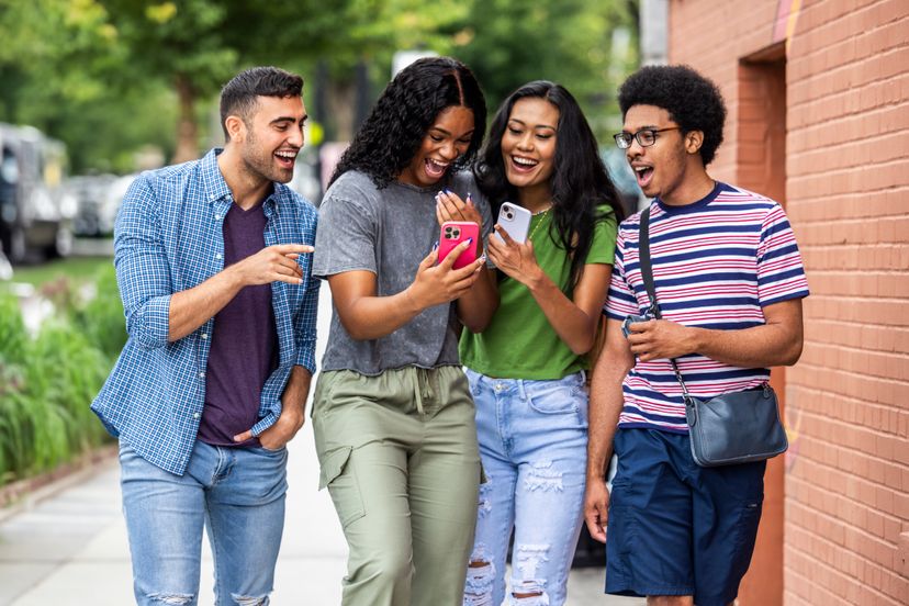 Group of young adult friends walking down urban street and using smartphone