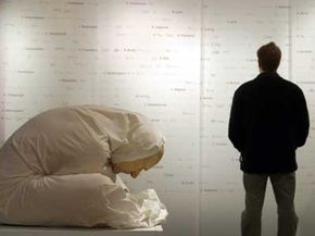 在柏林的医学历史博物馆，一名男子在观看一面墙，上面写着大约1万名纳粹实验受害者中的800人的名字，这是澳大利亚艺术家罗恩·穆克(Ron Mueck)创作的名为“裹着床单的人”的纪念碑。＂border=