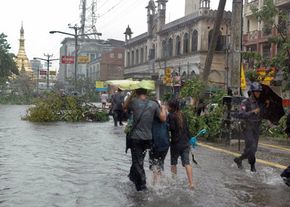 2008年5月3日，在缅甸最大的城市仰光，飓风过后，人们走在被洪水淹没的街道上(尽管那里称之为气旋)。＂border=