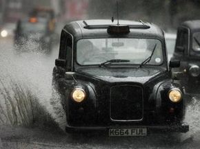 伦敦出租车驱动器通过一片死水,冒着湿路滑胎,倾盆大雨。”border=