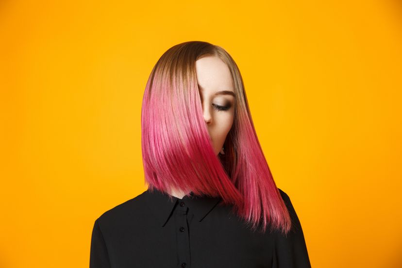 Studio shot of young colorful female on black blouse waving hair and isolated on orange.