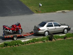 Car towing motorcycle on highway.