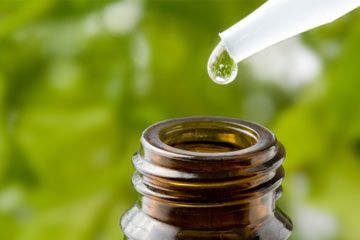 Macro shot of a pipette over a bottle, with fresh foliage in the background.