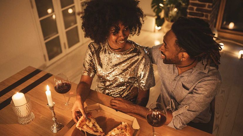 Young couple having romantic dinner at home. Eating pizza and drinking wine. Well dressed.