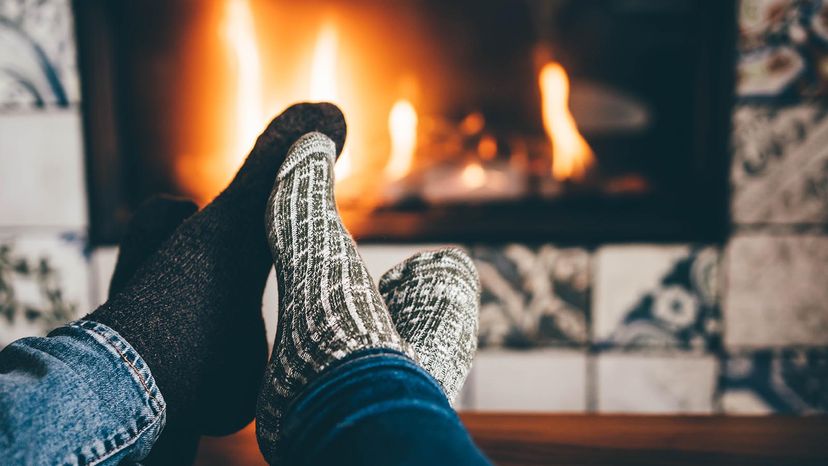 Couple warms their feet by the fireplace.