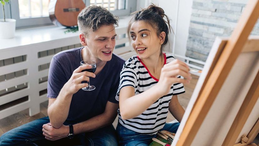 Girl painting at her living room and enjoying wine with her boyfriend.