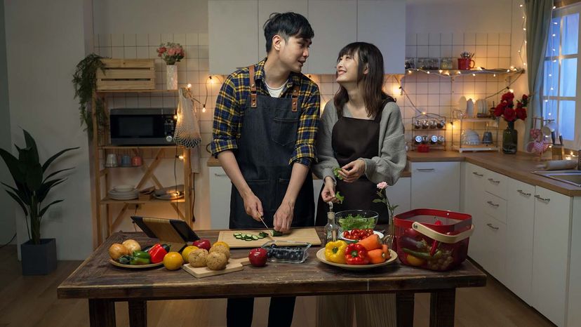 happy asian young couple working together making valentineâ€™s day dinner in a cozy decorated kitchen at home