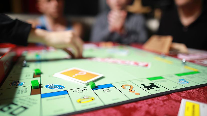 Group of people playing Monopoly board game together at night.Friends with funny emotions enjoying the game in evening.At home game. 