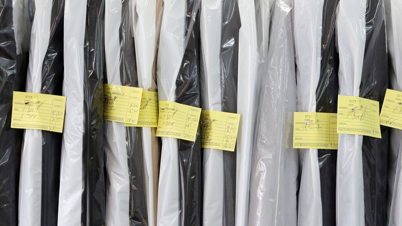 Plastic dry cleaning garment bags hanging up with yellow notes stapled to them.