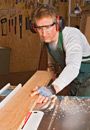 Carpenter sawing a board with a table saw in his woodworking shop. 