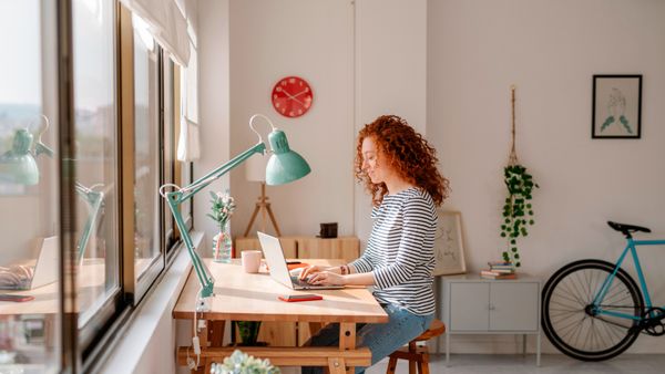 Woman sitting on a desk using a laptop computer while working from home.