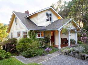 A pale yellow home surrounded in plants and flowers.