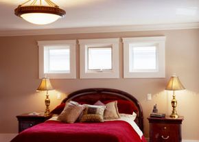 A bed with a red bedspread with three small windows above the headboard.