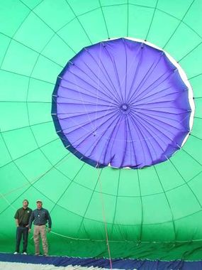 Two men stand in front of a purple and green hot air balloon parachute.