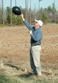 A man holding a small black balloon up above his head to check the wind direction.