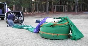 A man begins to set up a green and purple hot air balloon.