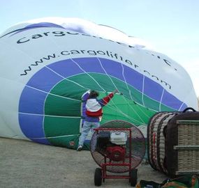 A man holds the balloon as it's being inflated using a large metal red fan.