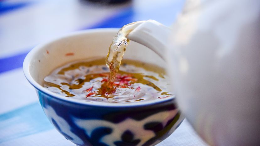 Serving saffron tea from pot into tea cup