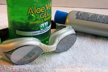 Swim goggles, suntan lotion and aloe vera gel on a towel.