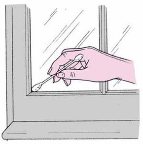 A hand holding a cotton swab to clean the corner of a window frame.