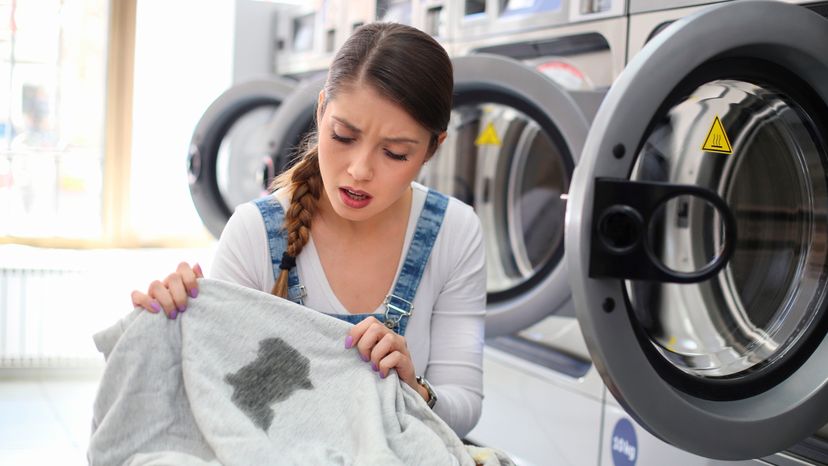 A young woman at a laundromat looking at a stain on her sweatshirt. 