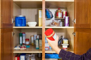 Close up of a woman's hand taking a jar of peanut butter out of an open pantry.