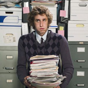Young man carrying stack of unorganized papers.