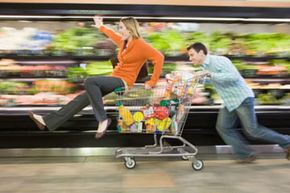 Man pushing woman in supermarket trolley down aisle, blurred motion