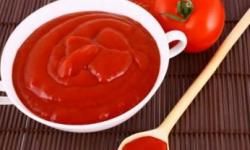 A bowl full of tomato sauce sat next to a wooden spoon and a tomato.&nbsp;