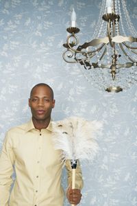 man holding a feather duster, standing below a chandelier