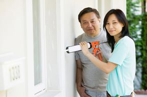 asian man and asian woman using caulk gun on house exterior