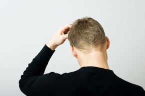 Man scratches head as viewed from behind.