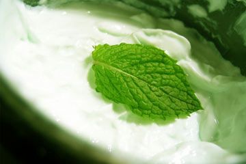 A fresh mint leaf sitting in a tub of mint body cream.