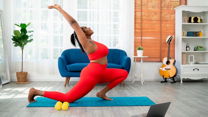 African young woman doing yoga virtual fitness class with laptop at home