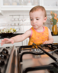 Child reaching their hand toward a the knob of a gas stovetop