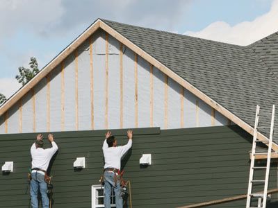 Workers installing siding on house.