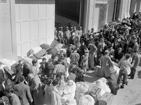 As military police stand guard, people of Japanese descent wait at a transport center in San Francisco on April 6, 1942, for relocation to an internment center at Santa Anita racetrack near Los Angeles.