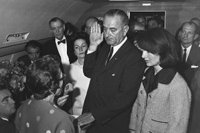 President Lyndon B. Johnson takes the oath of office aboard Air Force One after the assassination of John F. Kennedy. Kennedy's wife Jacqueline and Johnson's wife, Lady Bird, are by his side.