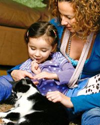 A mother and daughter pet a cat.