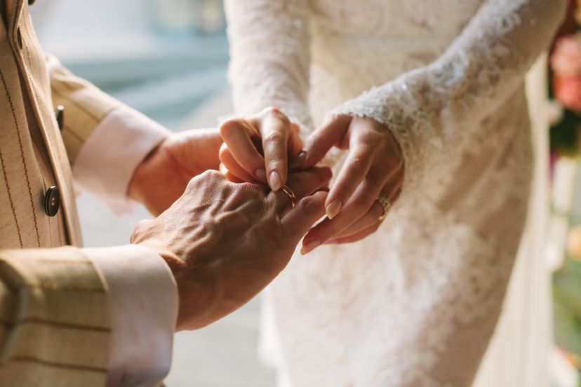 Bride putting ring on grooms finger. Rings exchange. Happy couple celebrating wedding outdoors in summer.