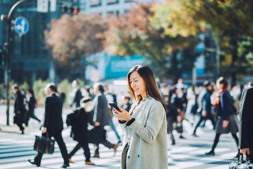 Young smiling lady using smartphone outdoors in busy downtown city street