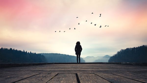 Woman standing on jetty and watching sunrise by the lake.