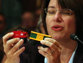 明尼苏达州民主党参议员克罗布彻(Amy Klobuchar)。，holds a toy train with lead paint as she testifies before Congress in 2007. U.S. lawmakers grilled the top executives of leading American toy companies following product safety scares tied to millions of Chinese-made toys.＂border=