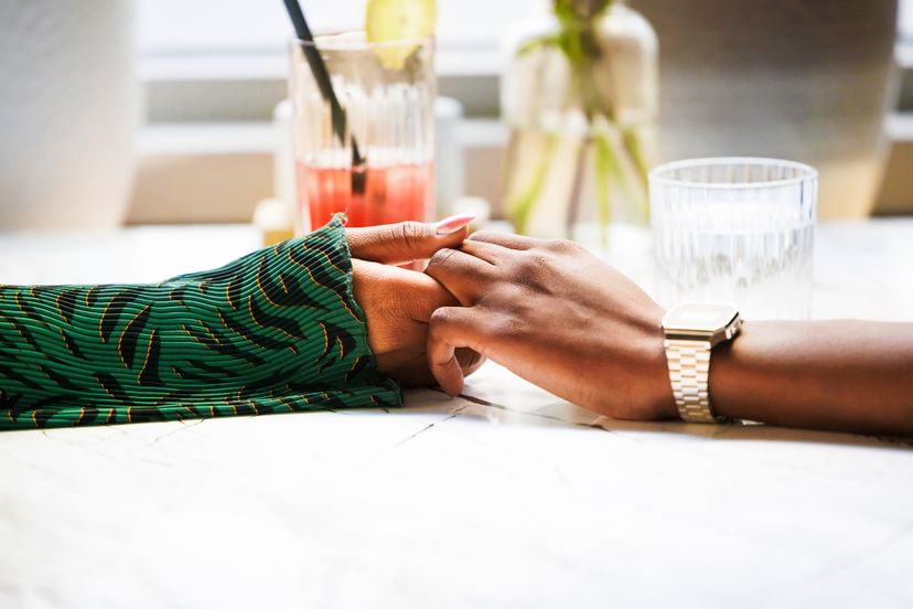 Two individuals hold hands across a table, conveying a sense of comfort and closeness in a relaxed setting.