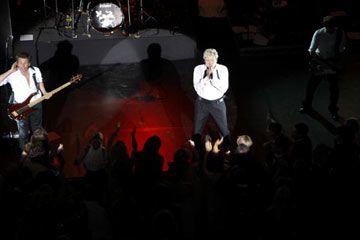 A singer strums a guitar on a stage in a performance group's performance space.