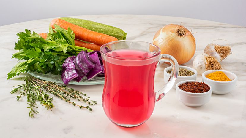A glass filled with red juice and different types of vegetables surrounding it on a table. 