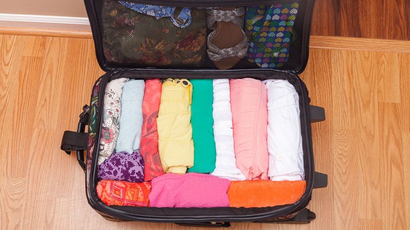 A suitcase with women's clothing packed by rolling the clothing,